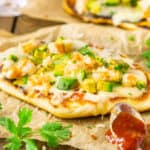 A shrimp and avocado grilled naan pizza on parchment paper with BBQ sauce.