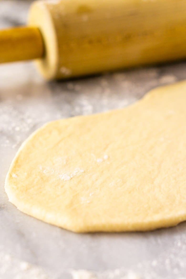 A piece of homemade garlic naan dough with a rolling pin.