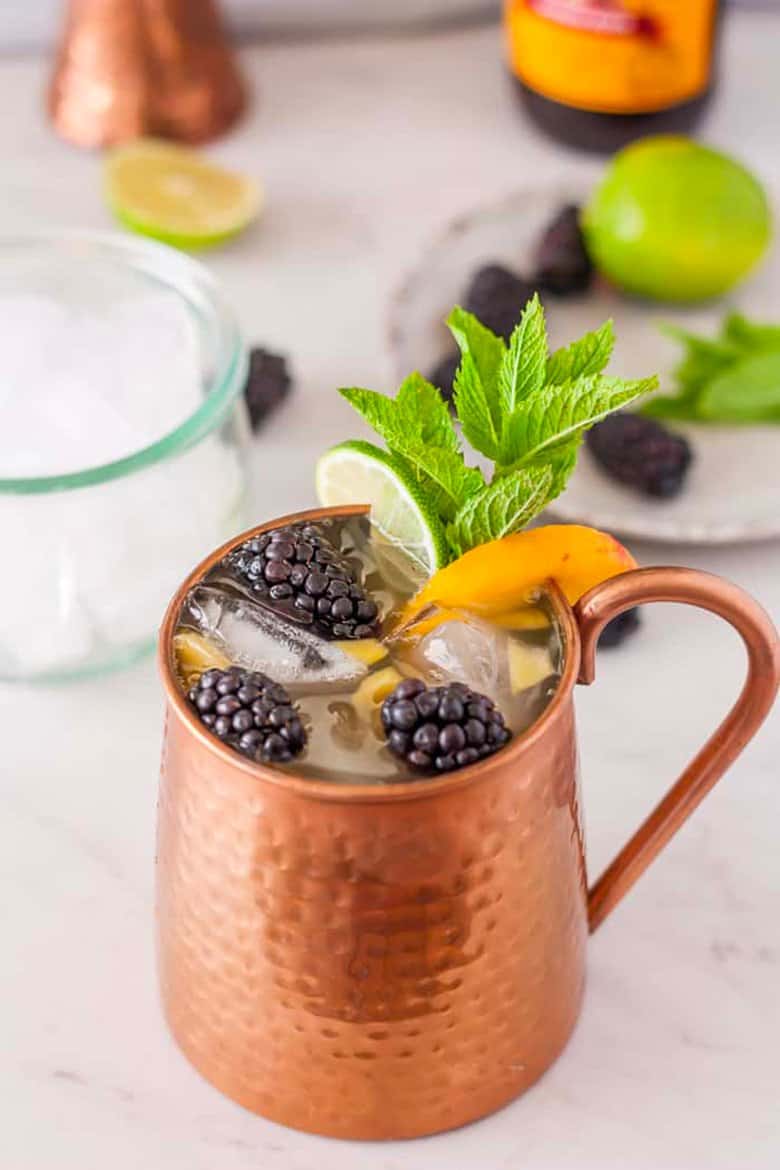 A peach Moscow mule with peaches and blackberries.