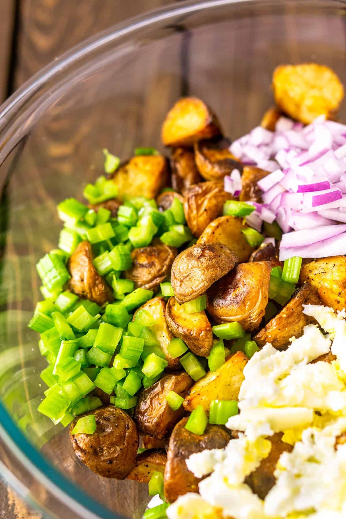 A bowl of roasted potatoes, celery, red onions and chopped eggs.