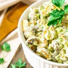 A bowl of herbed roasted potato salad with a serving spoon.
