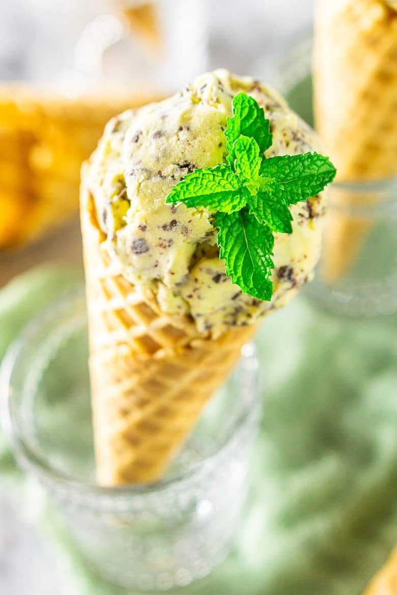 A close-up of a waffle cone with fresh mint-chocolate chip ice cream with a big mint leaf as a garnish.
