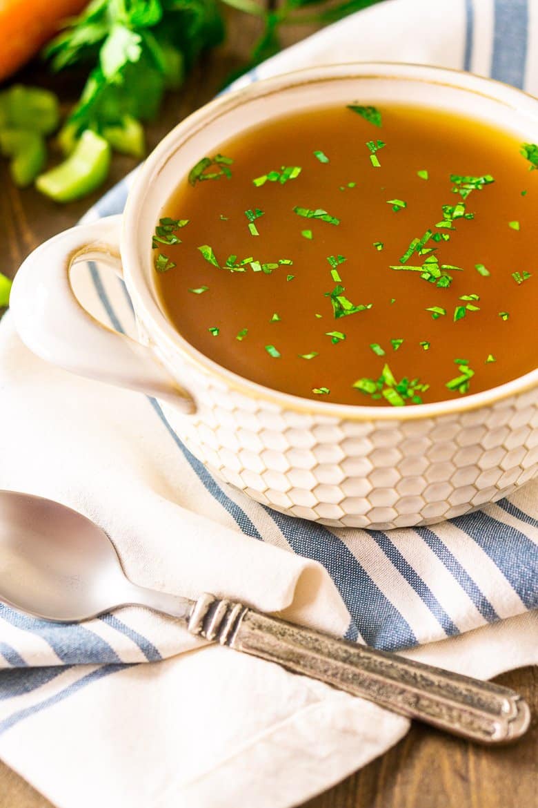 A bowl of homemade seafood stock with carrots and celery cut in the background.