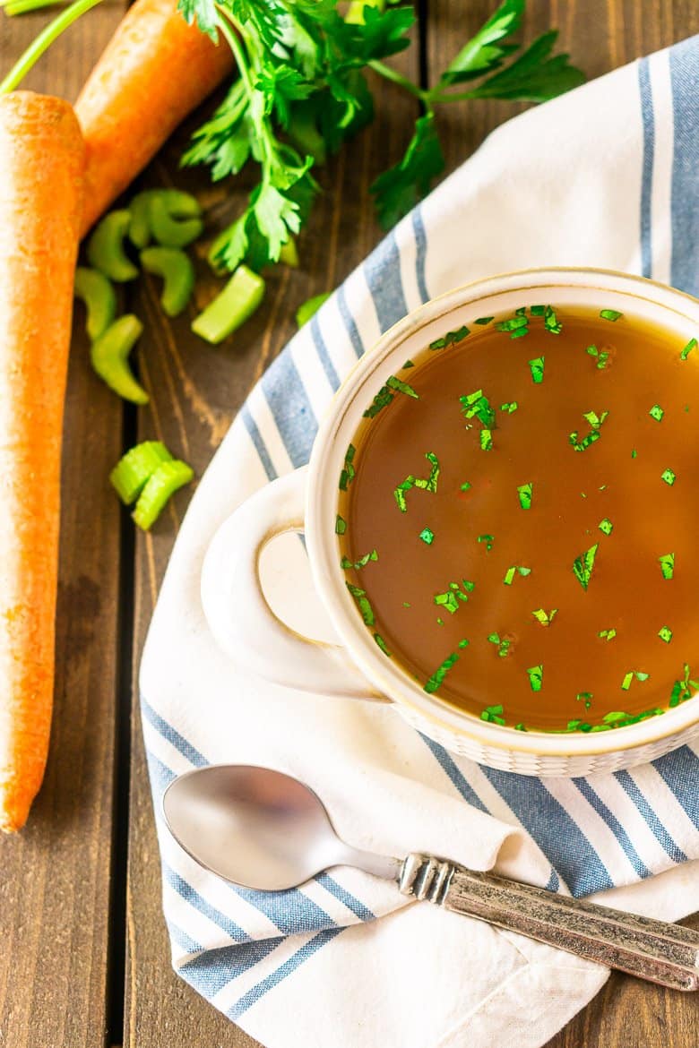 An aerial view of a bowl of homemade seafood stock on a napkin with a spoon.