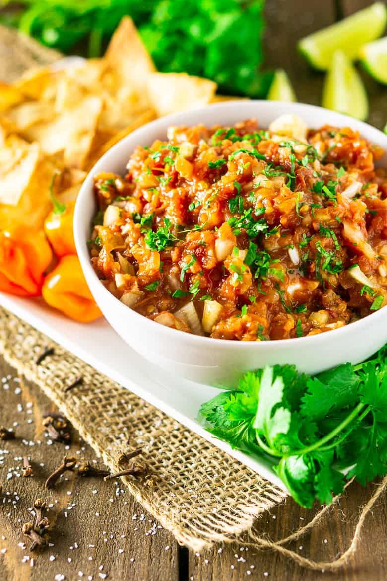 A bowl of Jamaican jerk salsa with chips and cilantro on a white plate.