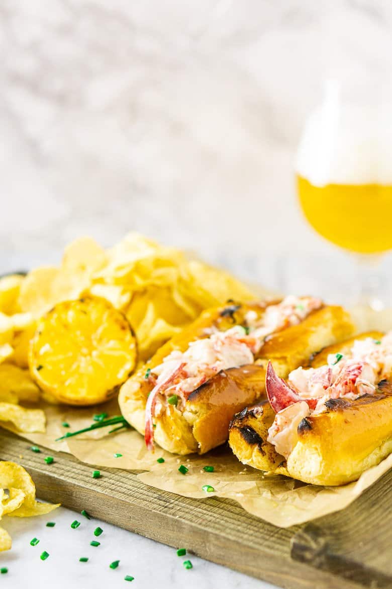 Two Maine-style lobster rolls on parchment paper with a beer in the background.