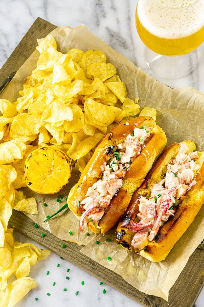 An aerial view of two Maine-style lobster rolls with a pile of chips and a beer.