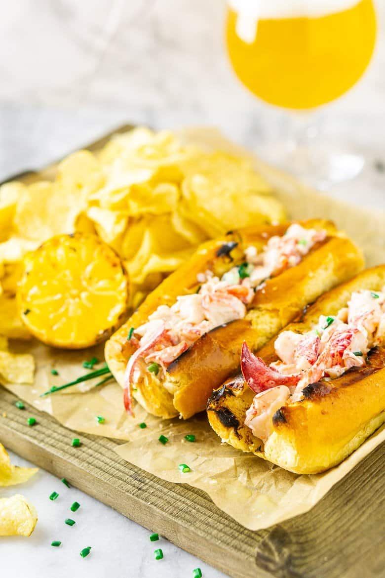 Two Maine-style lobster rolls on parchment paper and a wooden board ready to be served.