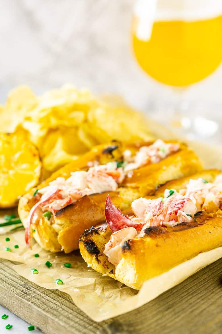 Two Maine-style lobster rolls with a pile of chips and lemon.