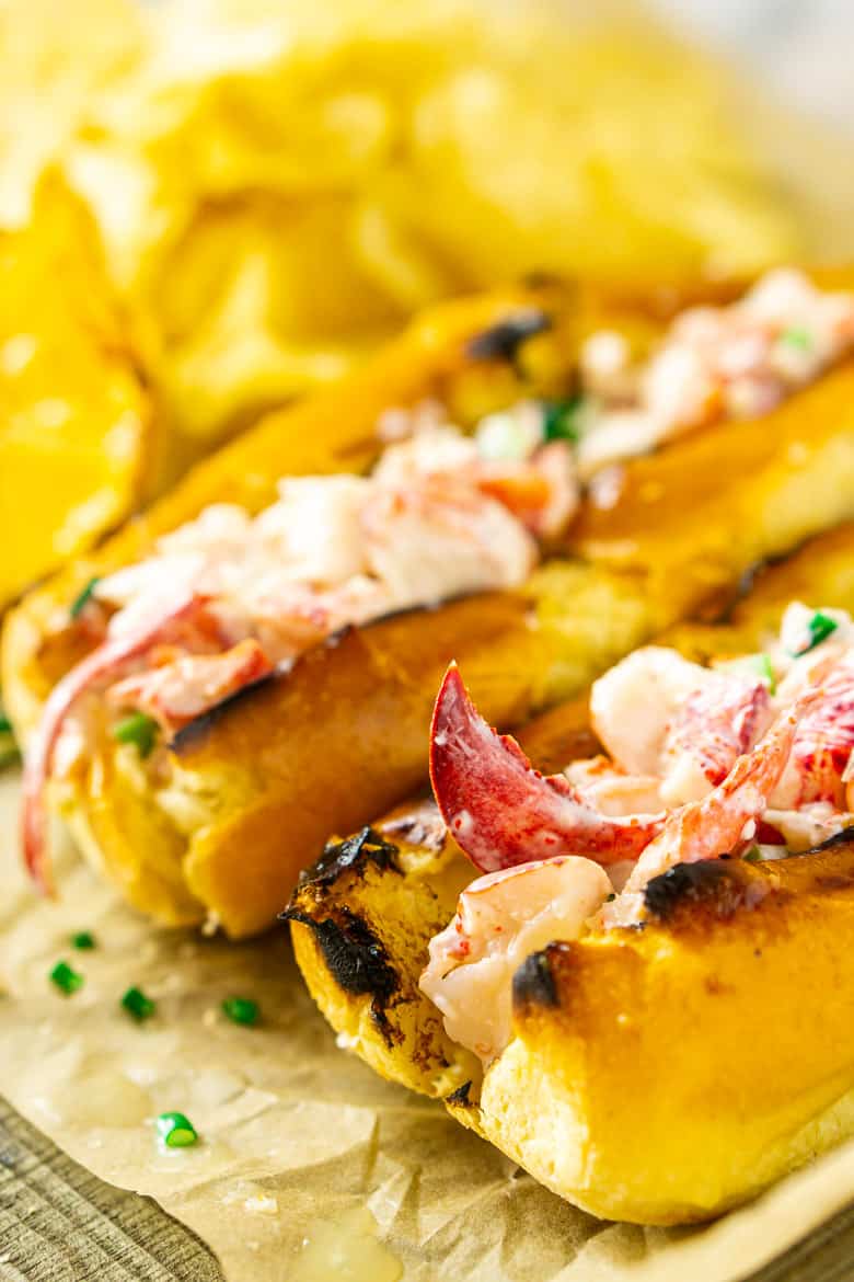 A close-up view of one Maine-style lobster roll with another in the background with chips.