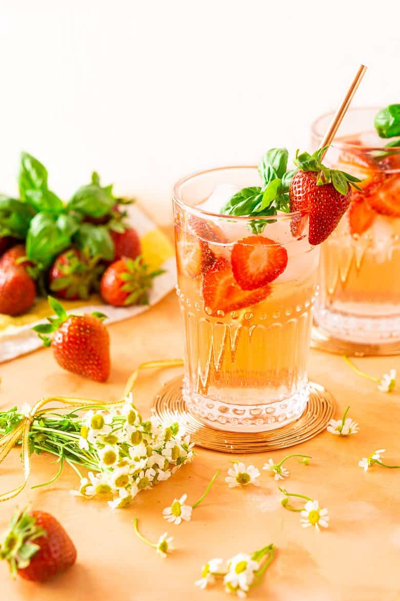 Two strawberry-basil Tom Collins drinks with flowers and strawberries.