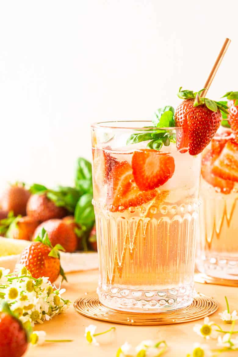 A close-up of a strawberry-basil Tom Collins with strawberries beside it.