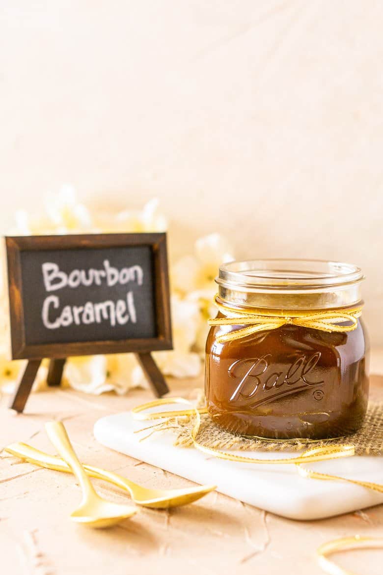 A straight-on shot of bourbon caramel sauce with a chalkboard sign and flowers in the background.