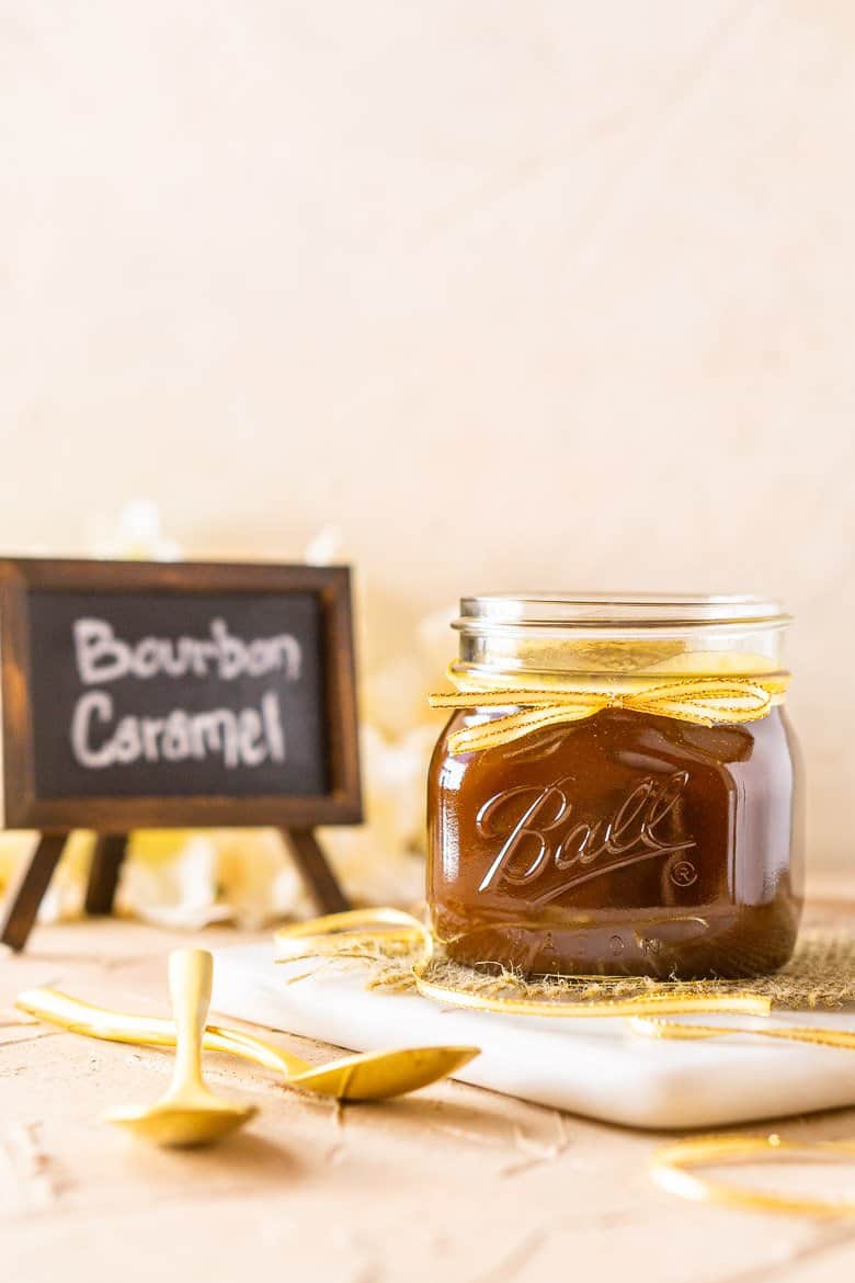 A jar of bourbon caramel sauce with a gold ribbon on a marble tray.