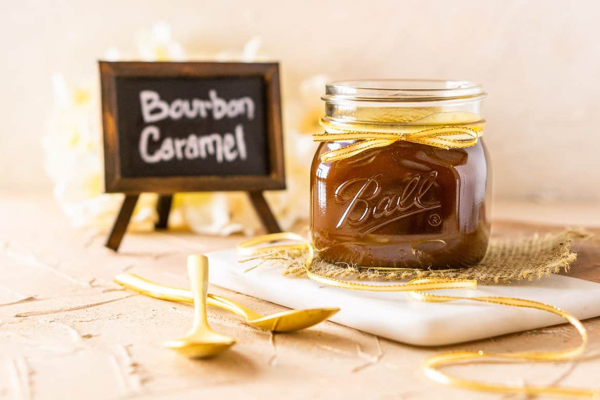 A jar of bourbon caramel sauce with two spoons and the chalkboard sign.