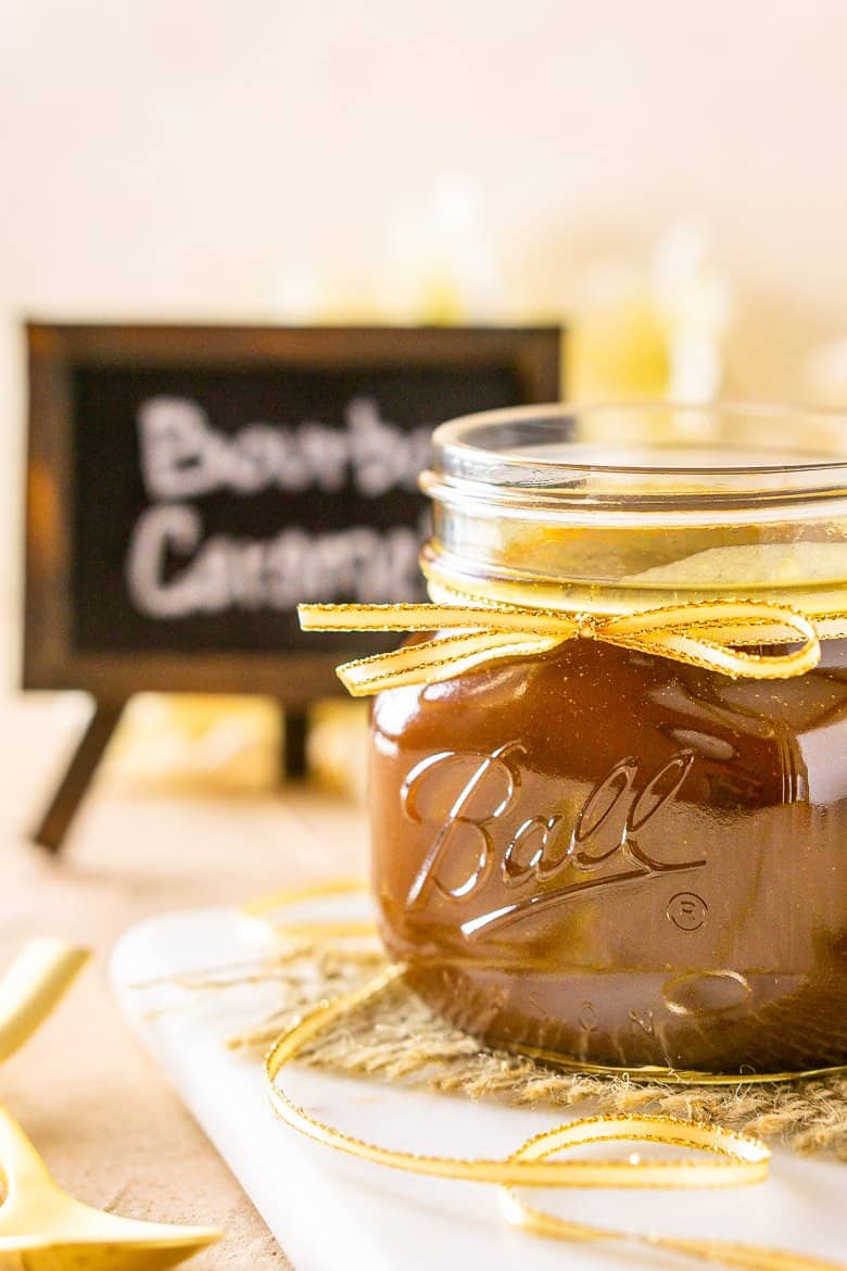 A jar of bourbon caramel sauce turned to the side on a marble tray.