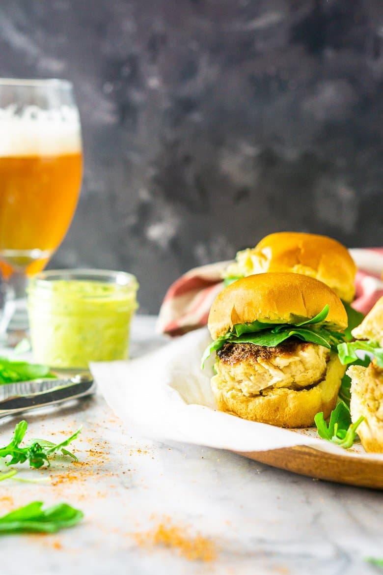 A platter of crab cake sliders with a beer in the background and a mason jar of basil-avocado aioli.