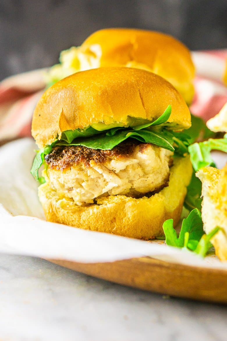 A close-up of a single crab cake slider on a tray.