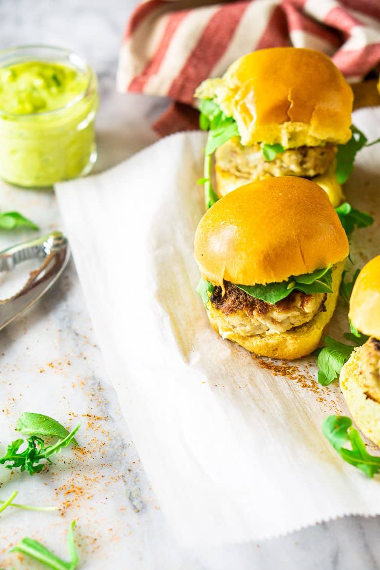 Looking down on a tray of crab cake sliders with a jar of basil-avocado aioli.