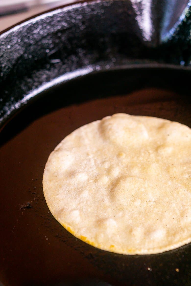 Lightly frying a corn tortilla in a cast-iron skillet.