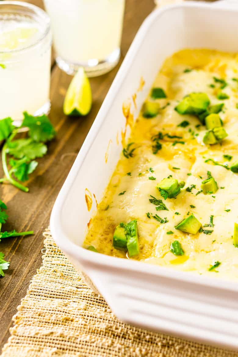 Looking down and to the side of a pan of jerk chicken enchiladas with cilantro and margaritas on the side.