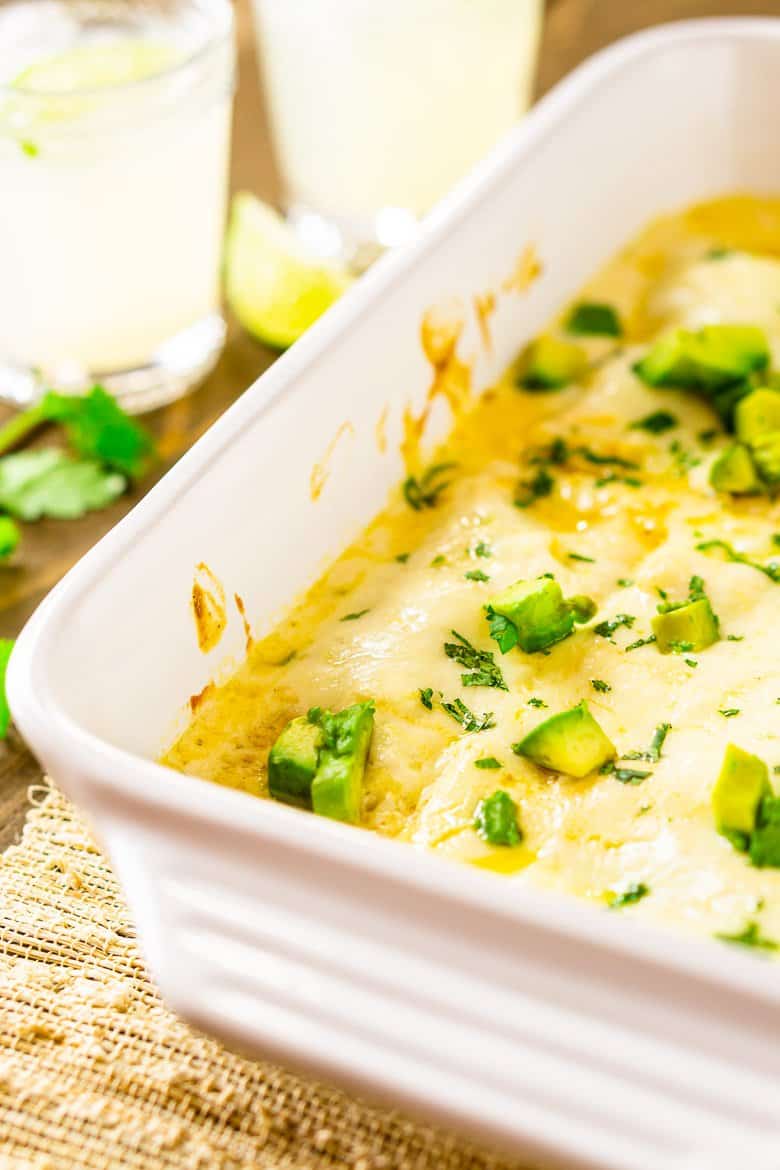A closer side view of a pan of jerk chicken enchiladas smothered in sour cream sauce.