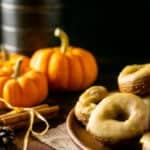 A plate of pumpkin crullers with caramelized maple glaze with pumpkins and fall flowers in the background.