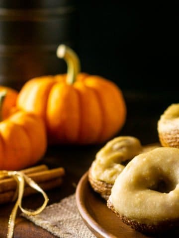 A plate of pumpkin crullers with caramelized maple glaze with pumpkins and fall flowers in the background.