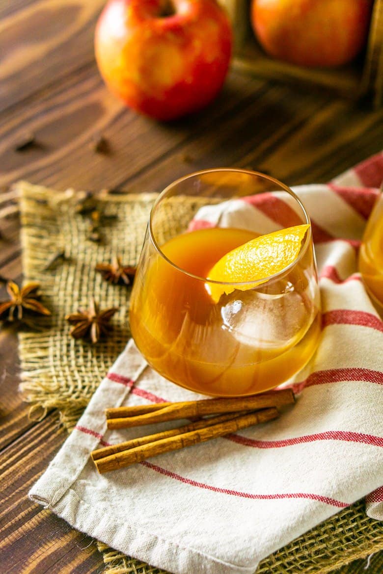 An apple cider old fashioned on burlap with spices.