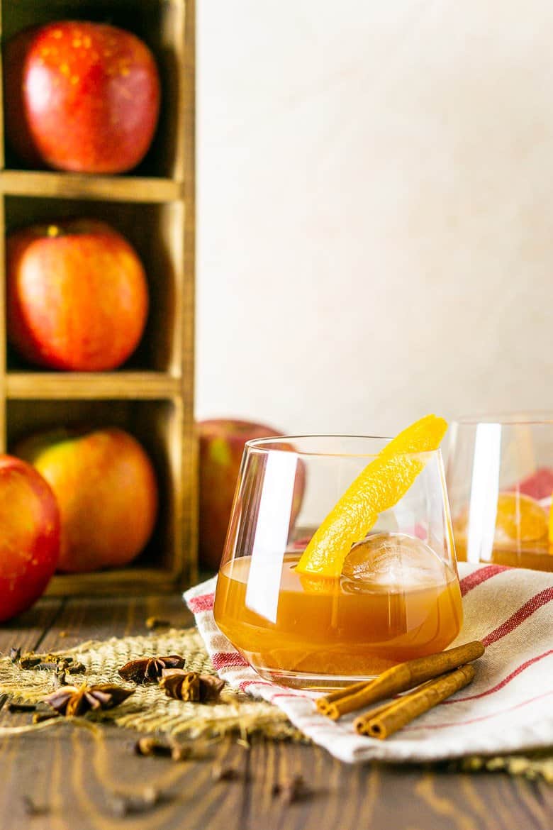 Looking straight on to an apple cider old fashioned with apples in the background.