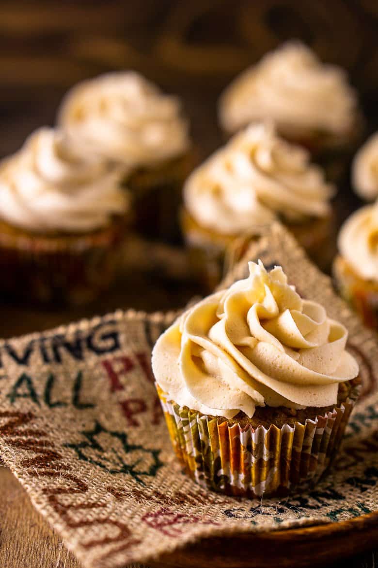 A close-up of a brown butter pumpkin cupcake on burlap and a wooden plate.