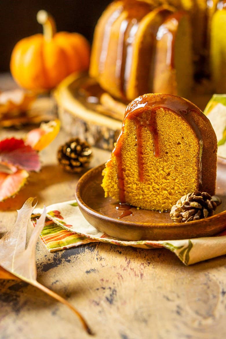 A slice of buttermilk-pumpkin pound cake on a wooden plate with the rest of the cake in the background.