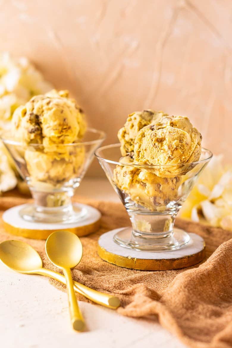 Two ice cream dishes of butterscotch ice cream with candied pecans on gold and marble coasters.