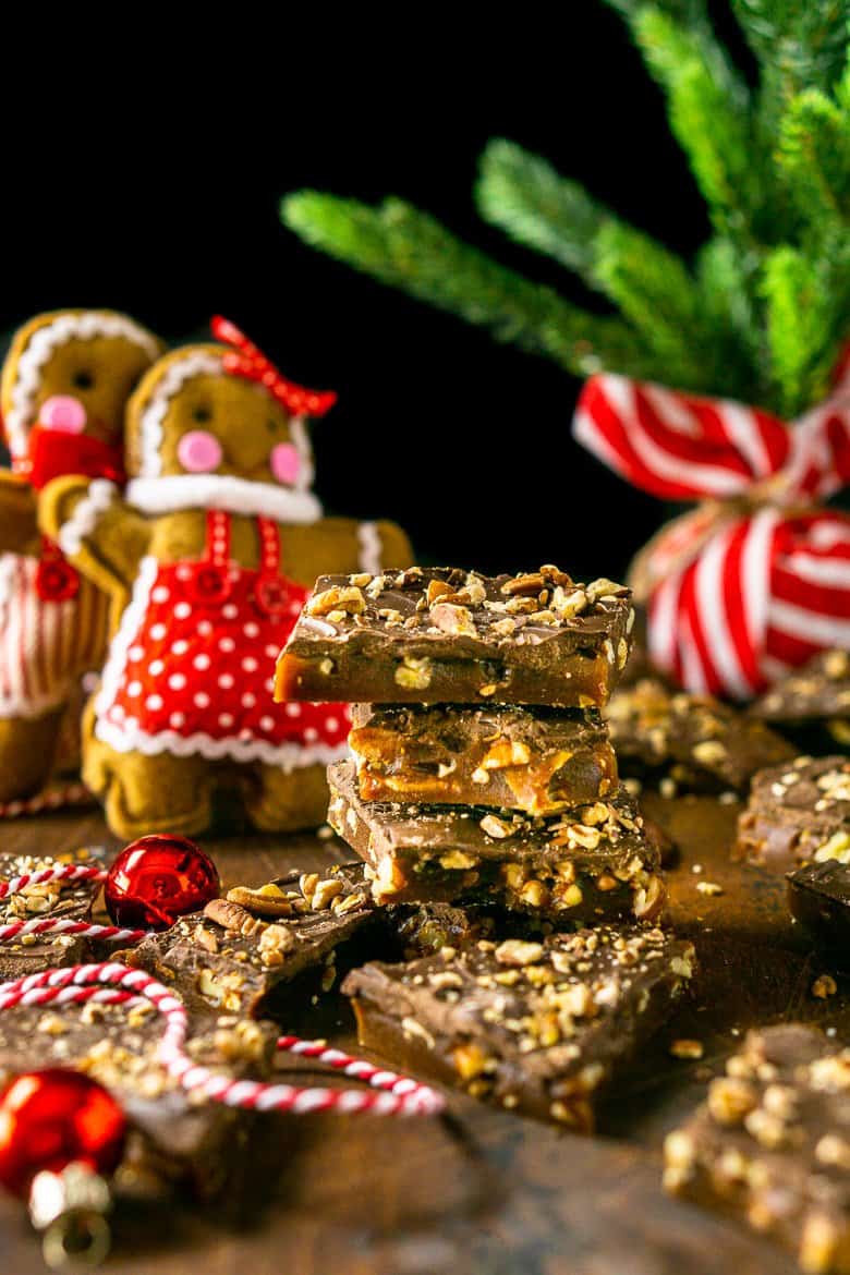 A stack of gingerbread toffee with gingerbread people ornaments and a small Christmas tree in the background.