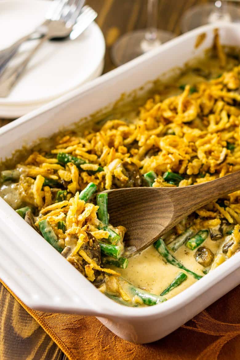A baking dish of homemade green bean casserole with a wooden serving spoon inside.