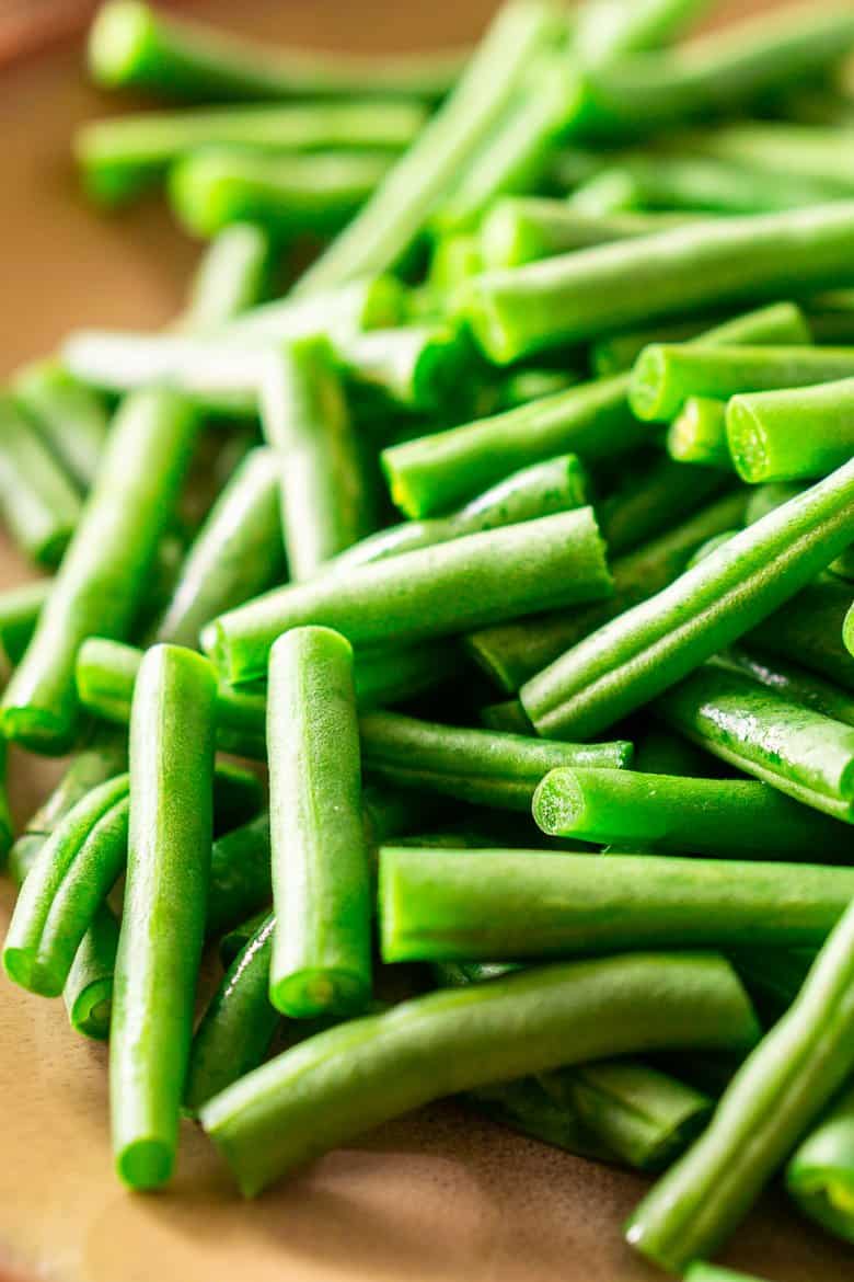 A pile of trimmed and cut fresh green beans on a wooden board.
