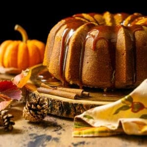 The buttermilk pumpkin pound cake on a wooden platter with fall decor around it.
