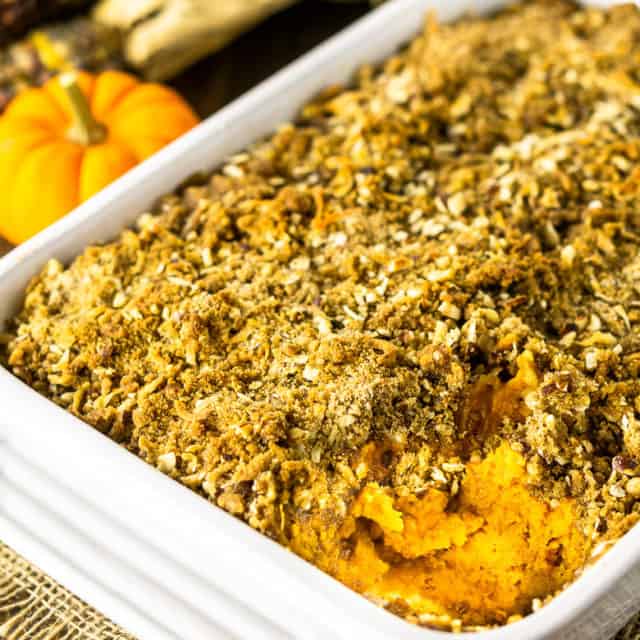 A baking dish of sweet potato souffle with coconut-hazelnut streusel with a pumpkin and Indian corn in the background.