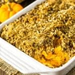 A baking dish of sweet potato souffle with coconut-hazelnut streusel with a pumpkin and Indian corn in the background.