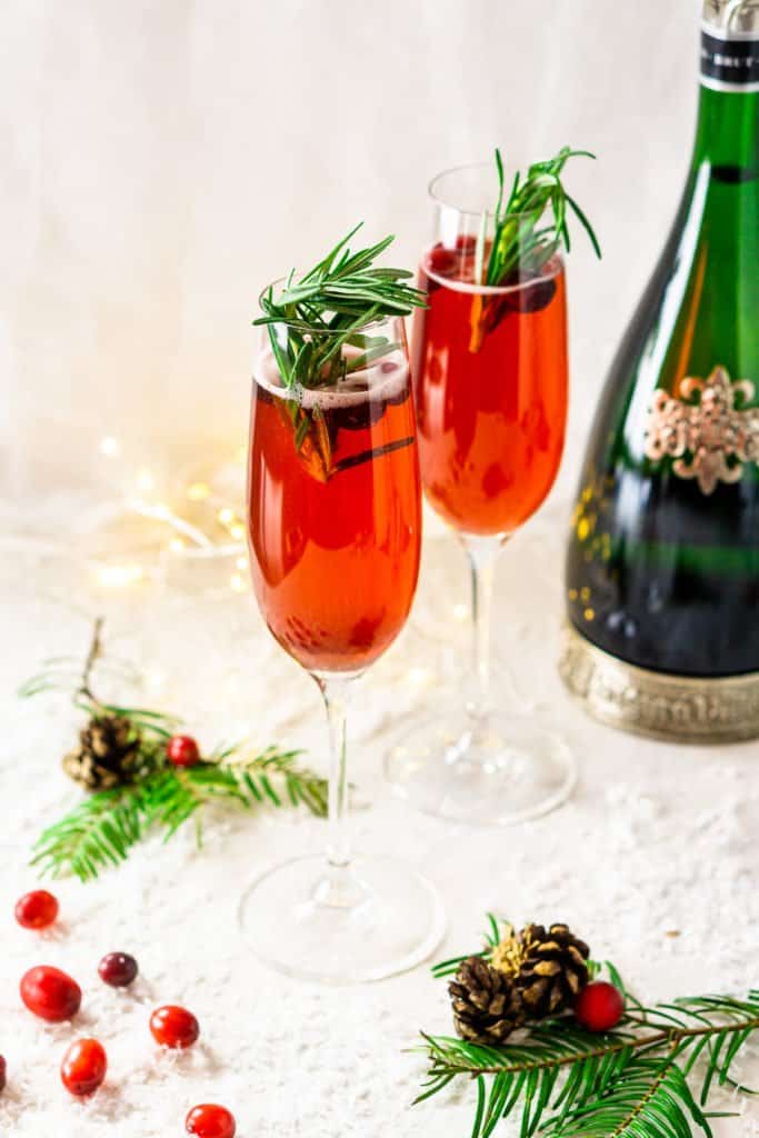 Two Christmas mimosas with pine leaves and fresh cranberries and fake snow.