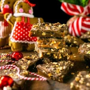 A stack of gingerbread toffee with gingerbread people ornaments and a small Christmas tree in the background.