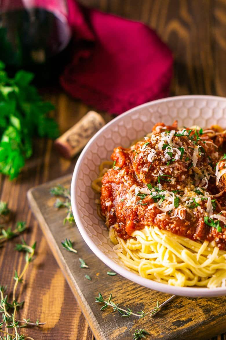 A bowl of Italian meatballs and spaghetti with fresh thyme around it on a wooden board.