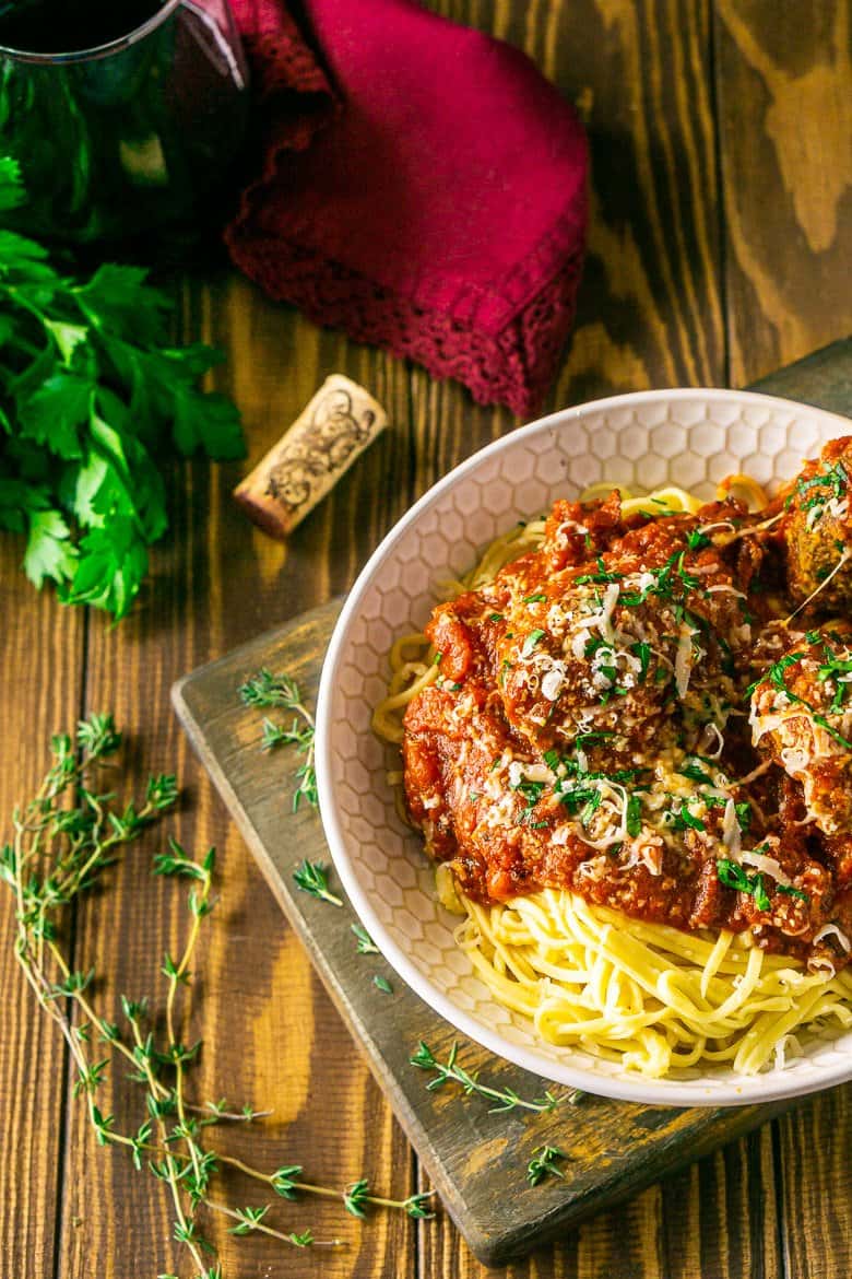 An aerial view of Italian meatballs and spaghetti with fresh herbs around it.