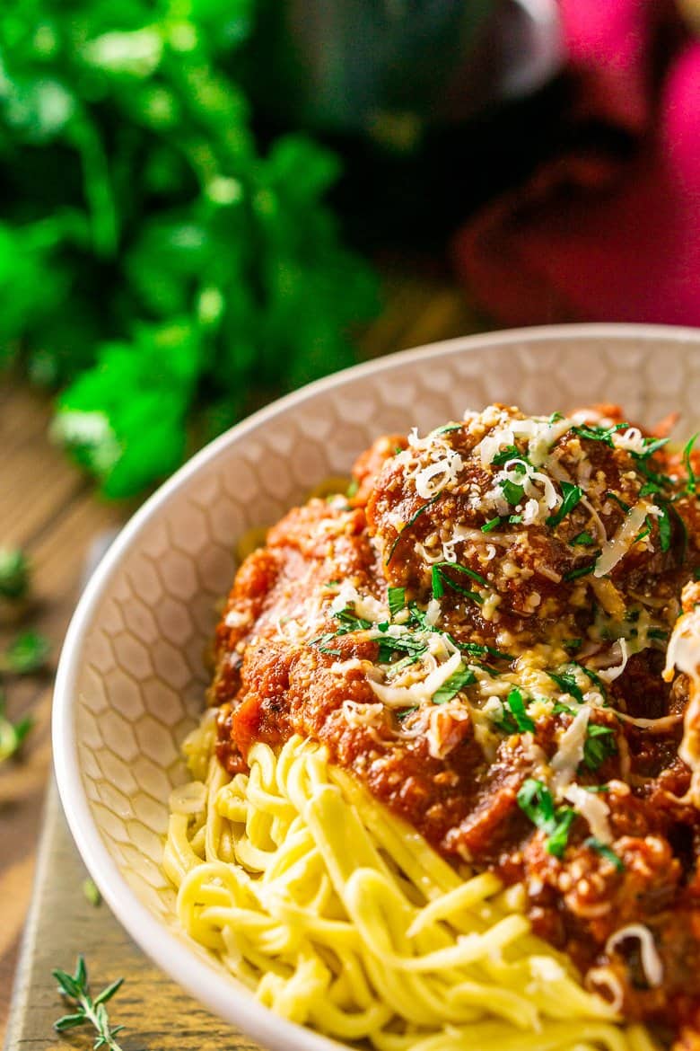 A close-up shot of a bowl of Italian meatballs and spaghetti with a bunch of fresh parsley.