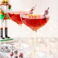 Two Sugar Plum Fairy Martinis on a marble board with a nutcracker and lights behind them.
