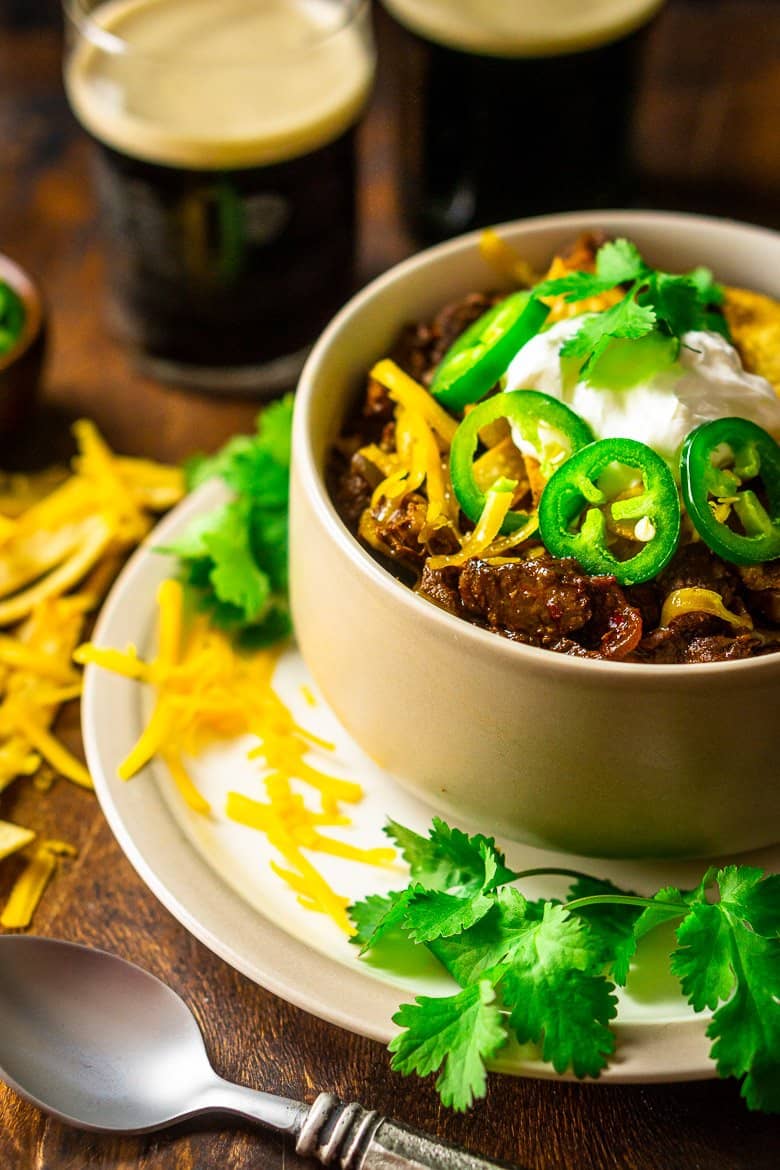 A bowl of red chili on a small plate with a spoon and grated cheese on the side.