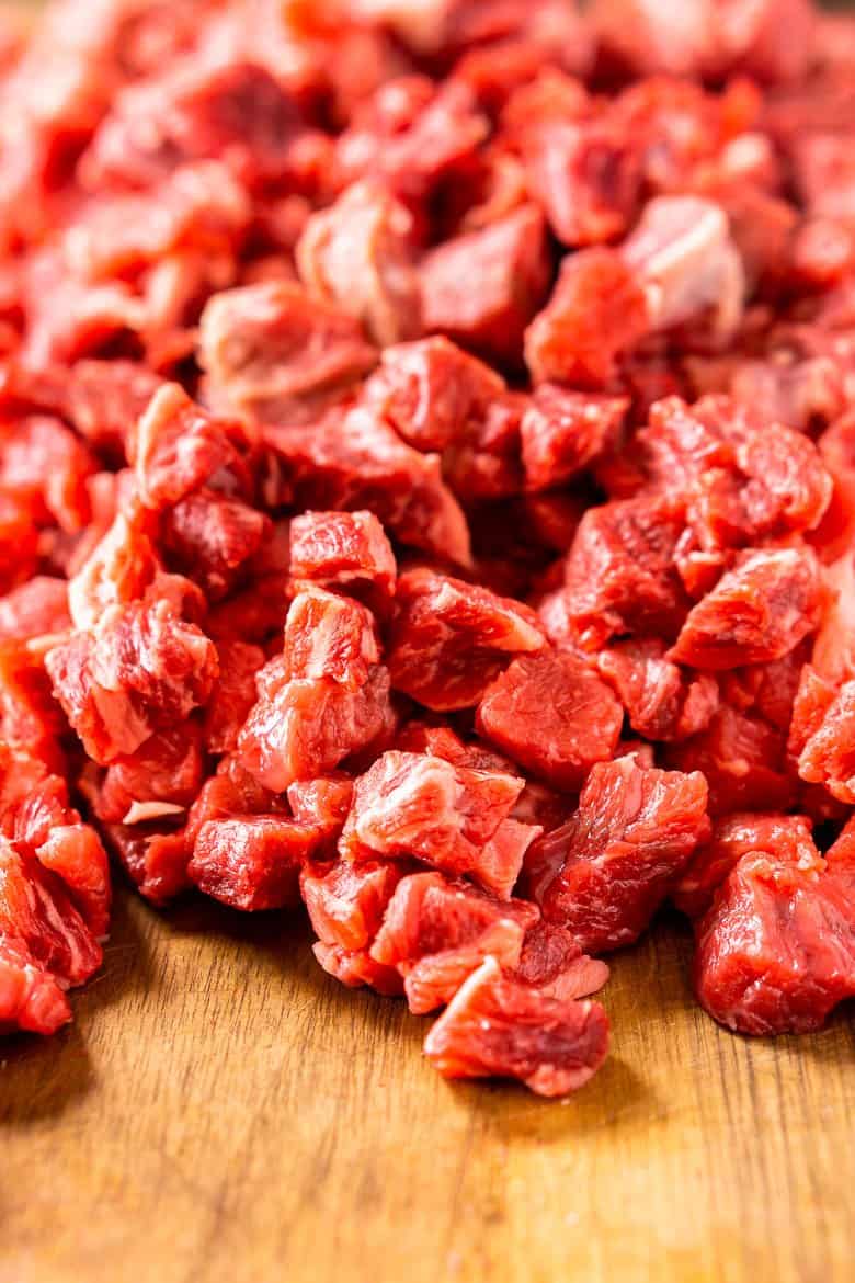 Chuck roast cut into small pieces on a wooden cutting board.