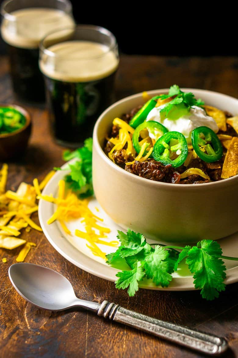 Texas chili in a bowl with a spoon on the side and a bowl of sliced jalapenos.