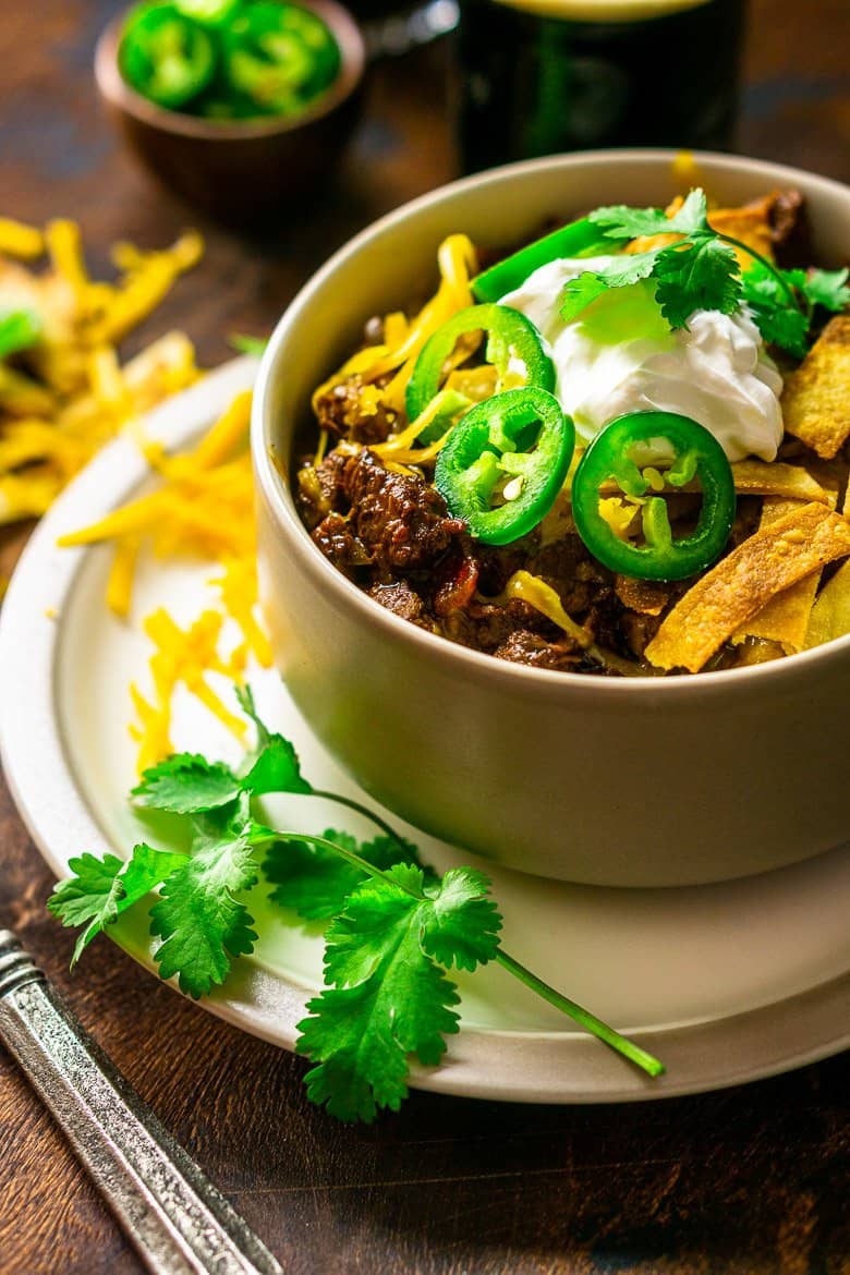 A bowl of chili on a plate with shredded cheese next to it.