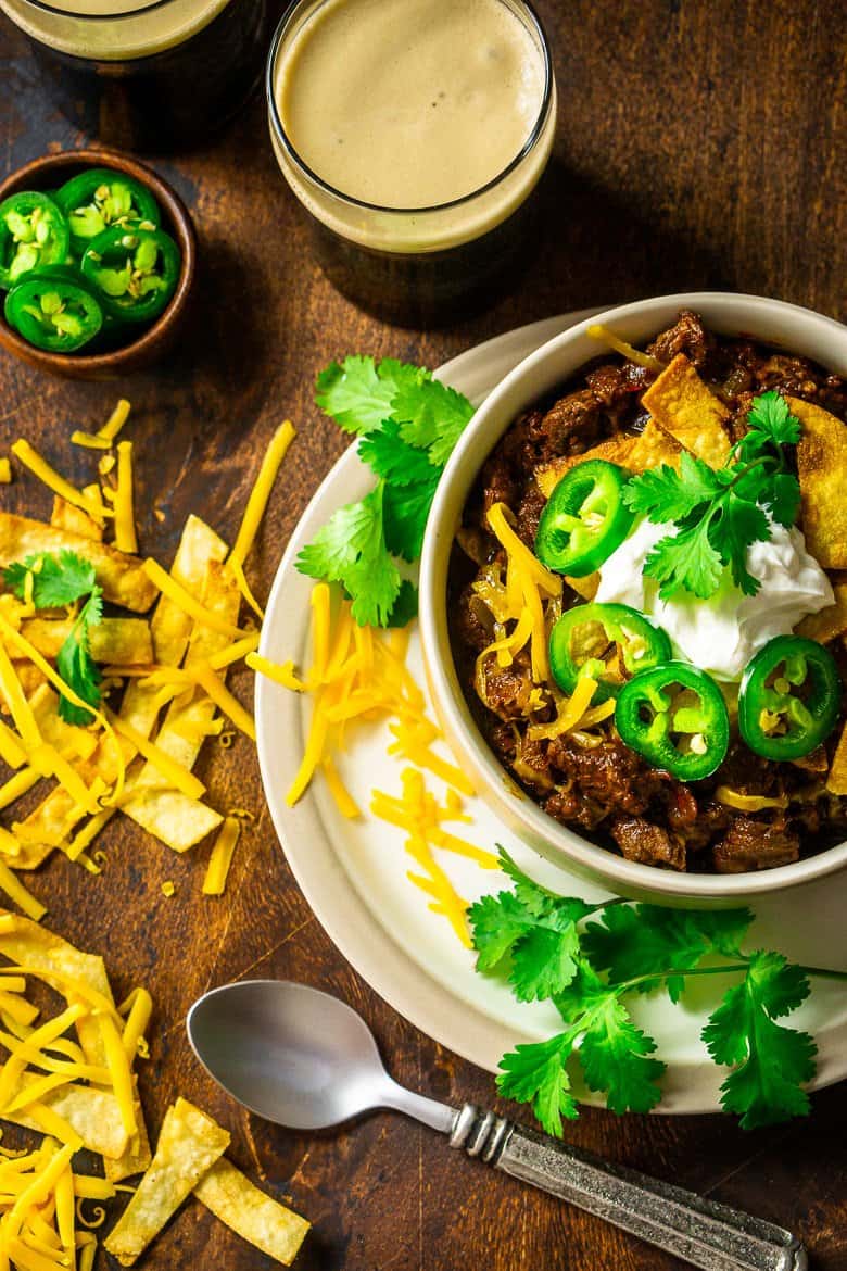 An aerial view of the bowl of red chili with cheese, cilantro and two stouts on the side.